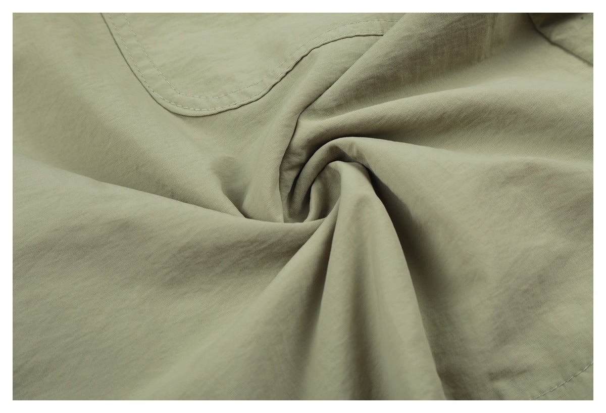 Close-up of sage-green shorts fabric gathered into folds, with part of a curved stitched pocket.