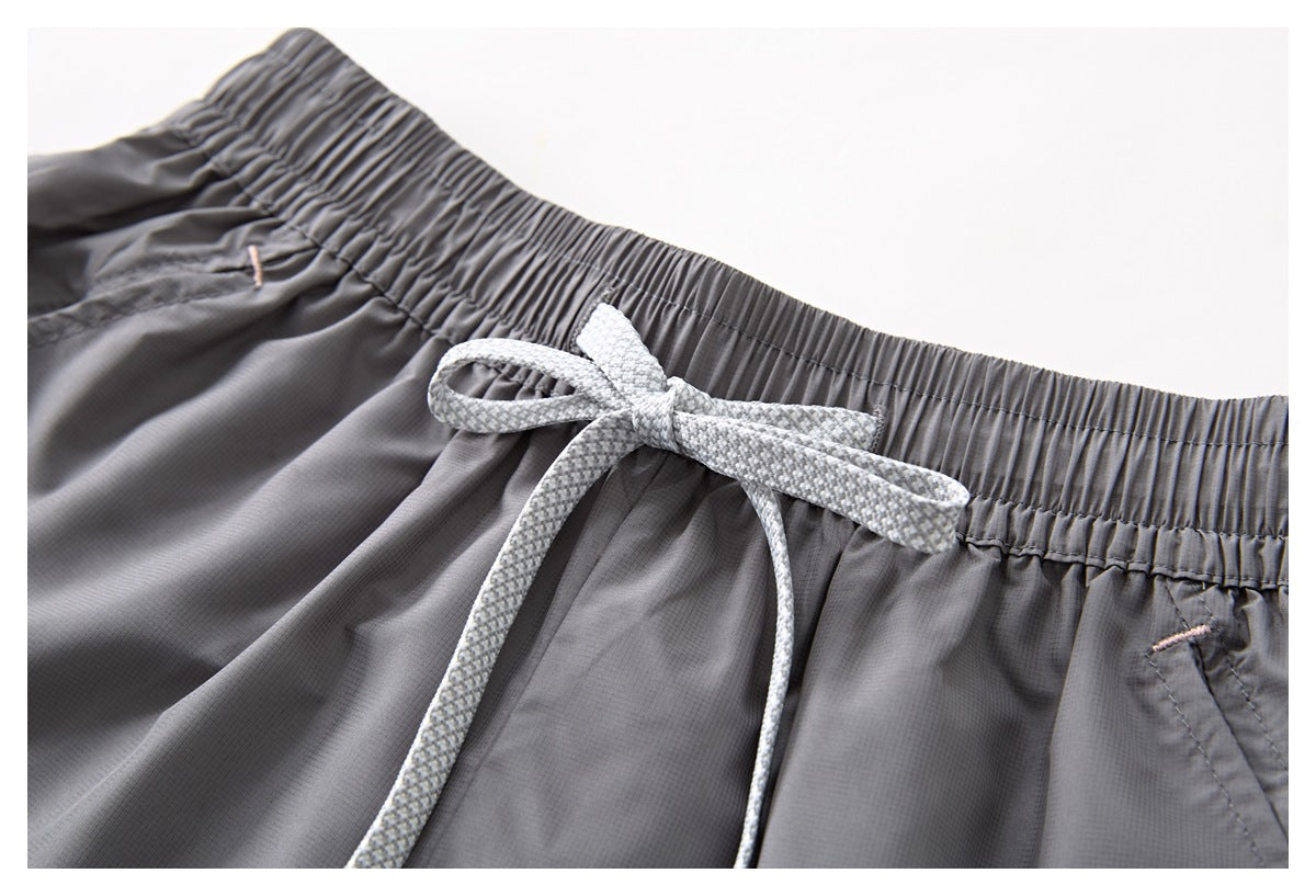 Close-up of the white patterned drawstring tied at the gathered waist of gray shorts.