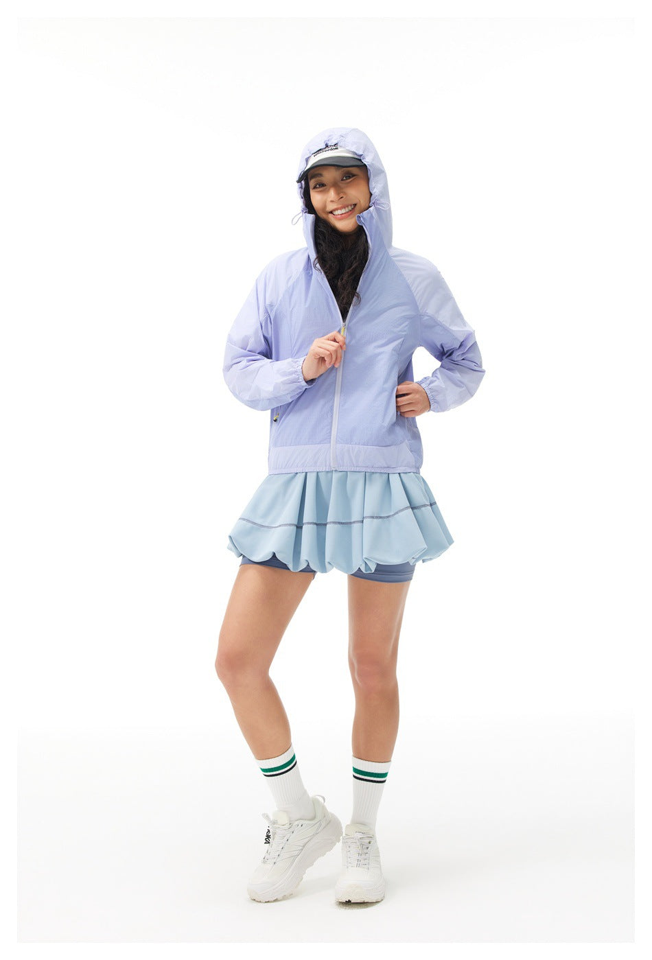 Woman wearing a lavender hooded jacket over a pale blue ruffled athletic skirt and shorts.