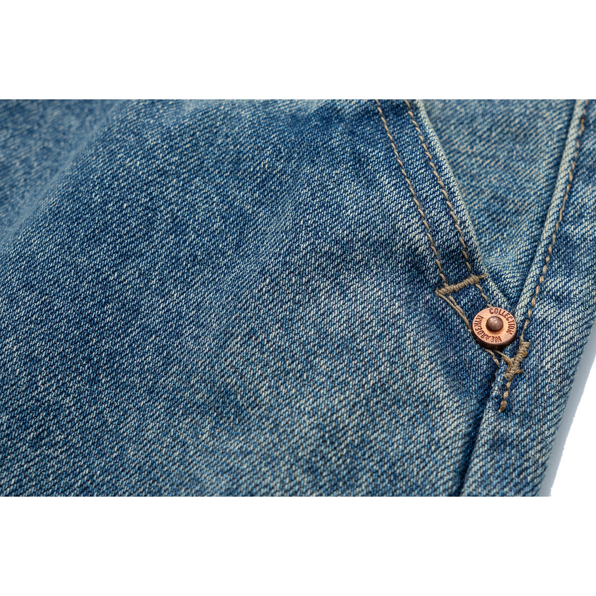 Close-up of blue denim stitching and a copper-tone rivet with small lettering.