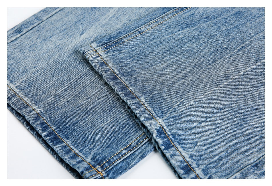 Close-up of blue washed denim showing a folded hem and parallel rows of golden stitching.