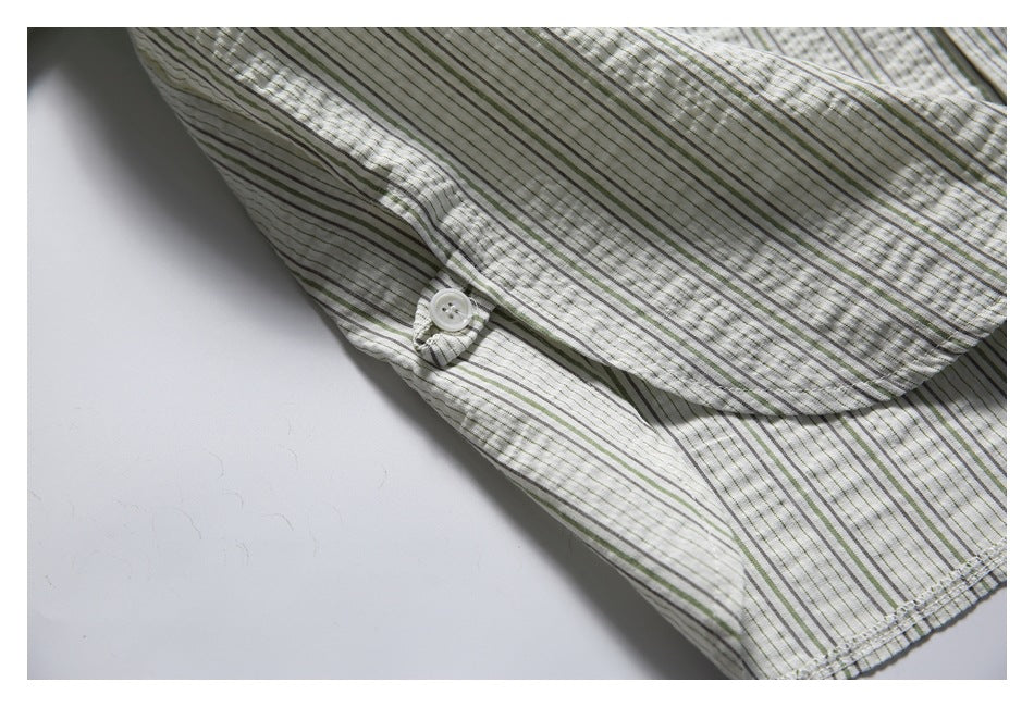 Close-up of a white striped shirt showing a small white button and overlapping fabric panels.