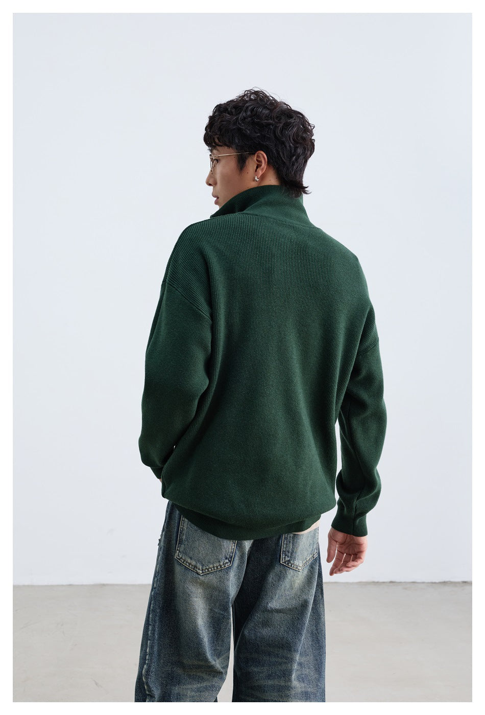 Model seen from behind wearing a dark green high-collar pullover with jeans.