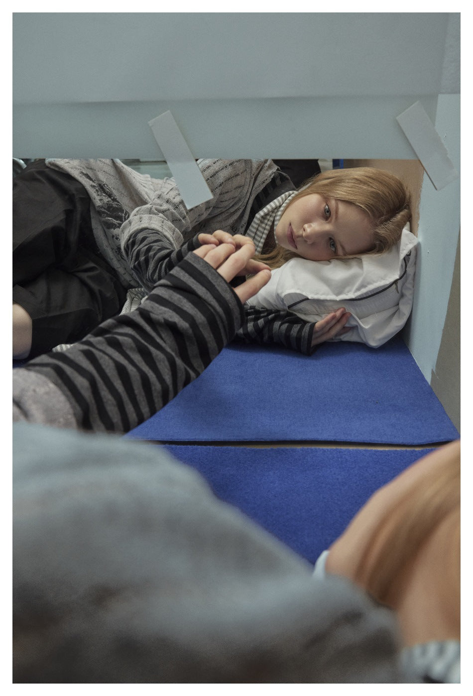 Model reclining in a gray graphic T-shirt layered over a dark striped long-sleeve top and black shorts.