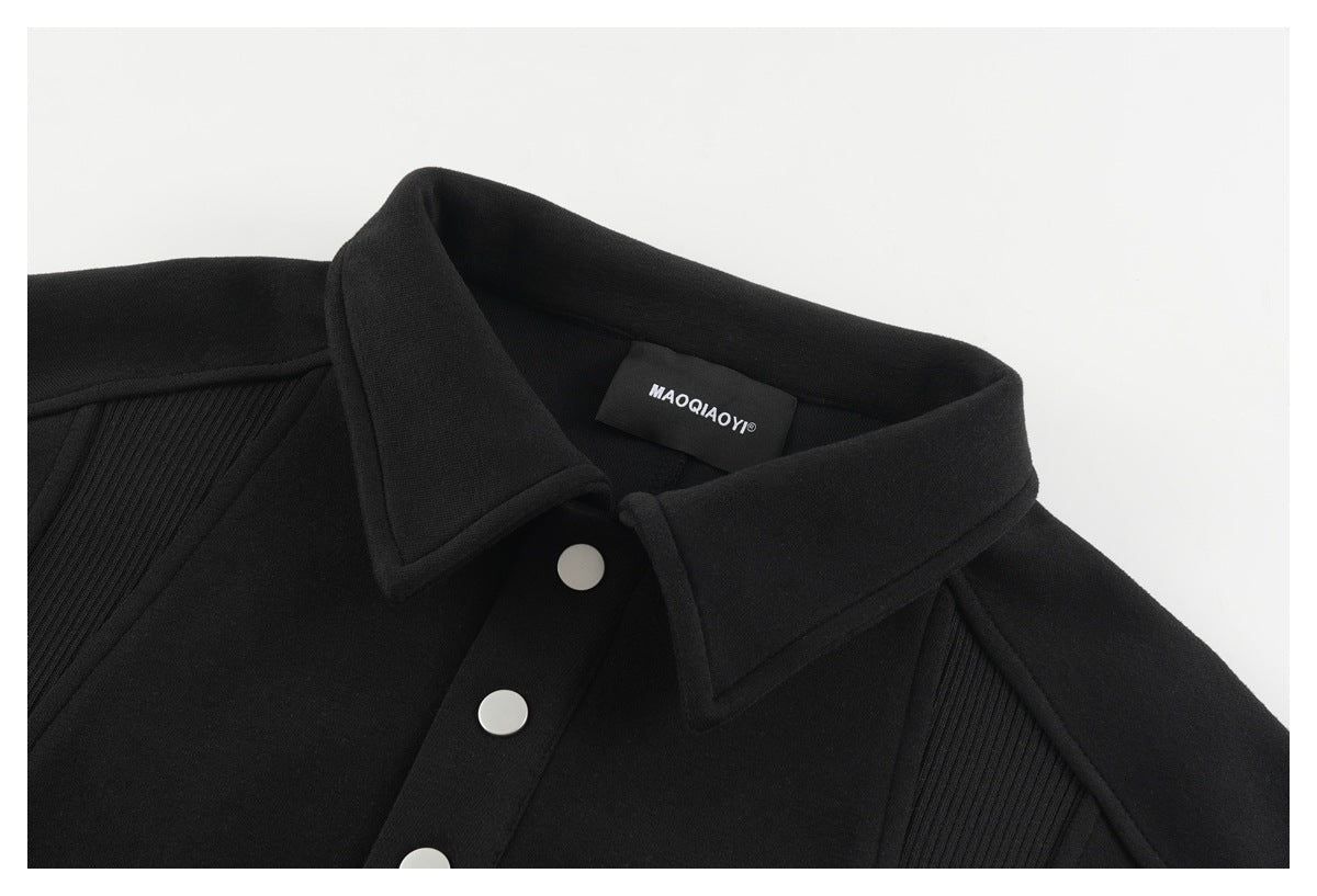 Close-up of a black collared sweatshirt with silver snap buttons and ribbed shoulder panels.
