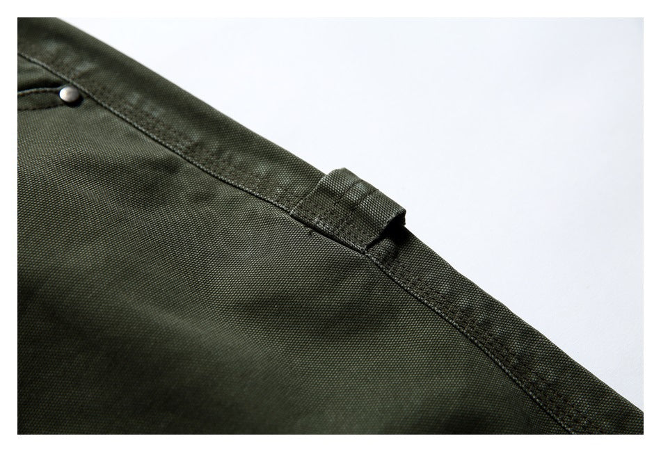 Close-up of olive trousers showing a belt loop, waistband seam and metal rivet.