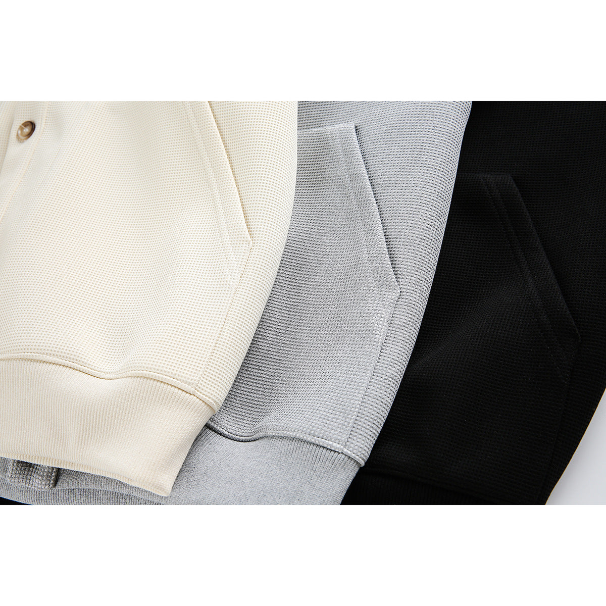 Close-up of cream, gray, and black jackets showing textured fabric, seams, and ribbed hems.