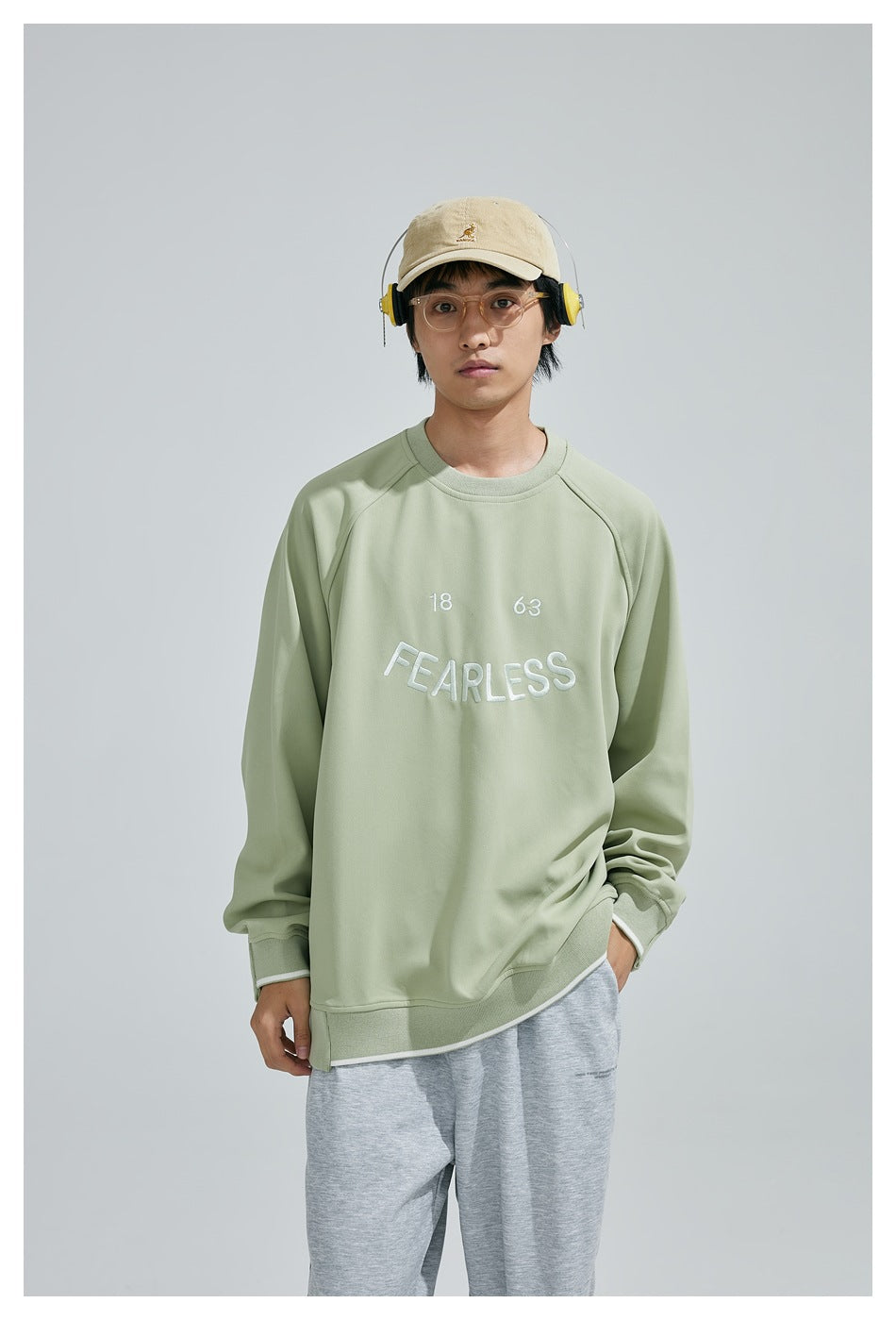 Fuller front view of a model wearing a sage-green sweatshirt with white “18 63 FEARLESS” embroidery.