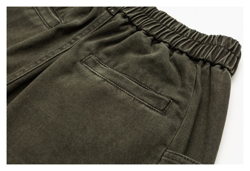 Close-up of dark olive trousers showing the elastic waistband, slanted pocket and side utility pocket.