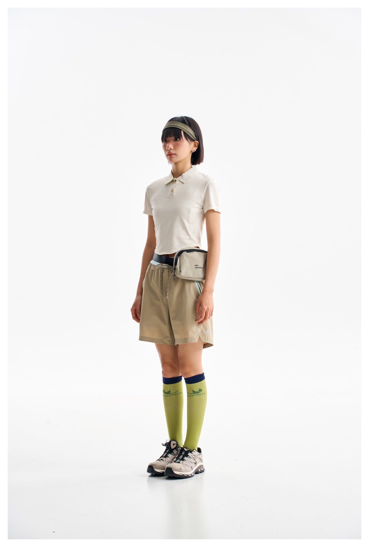 Model wearing an ivory short-sleeve polo shirt and tan drawstring shorts with a small waist bag.