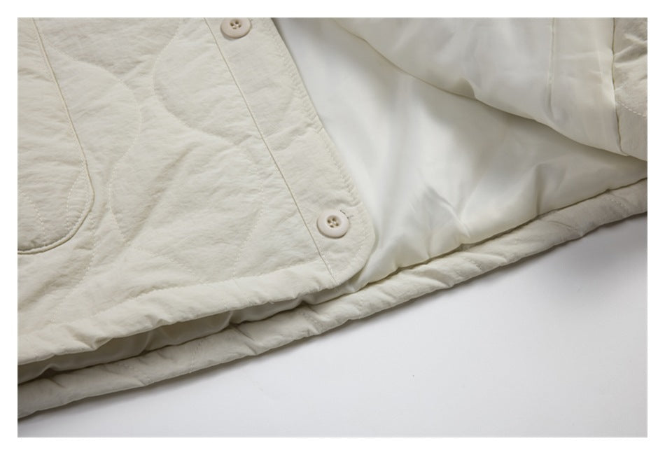 Close-up of the ivory quilted jacket's button front, pocket edge, and smooth pale lining.