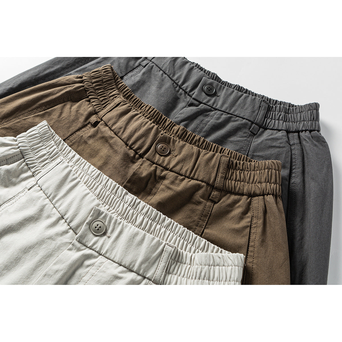 Close-up of three wide-leg trousers in light gray, brown, and charcoal, showing elastic waistbands and buttons.