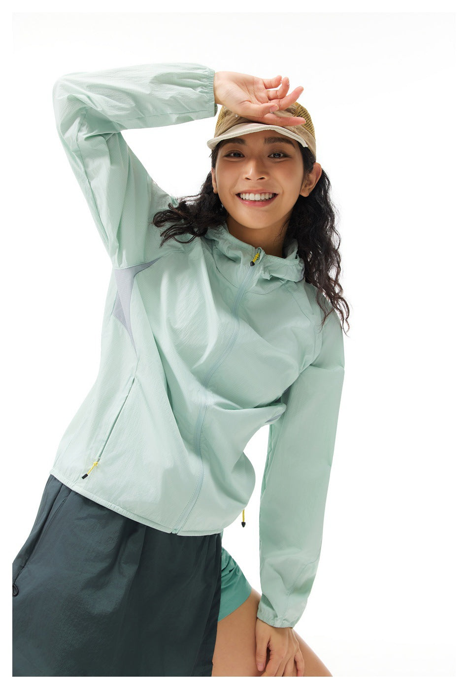 Close view of a model in a pale mint hooded jacket, showing its front zipper, hood, and yellow pocket pulls.
