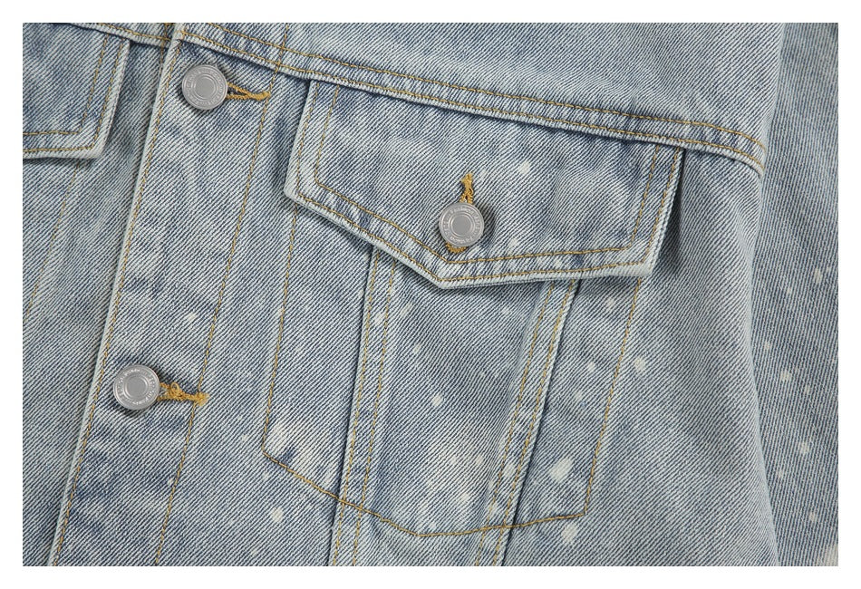 Close-up of a light blue acid-wash denim jacket with flap pockets, silver buttons and tan stitching.