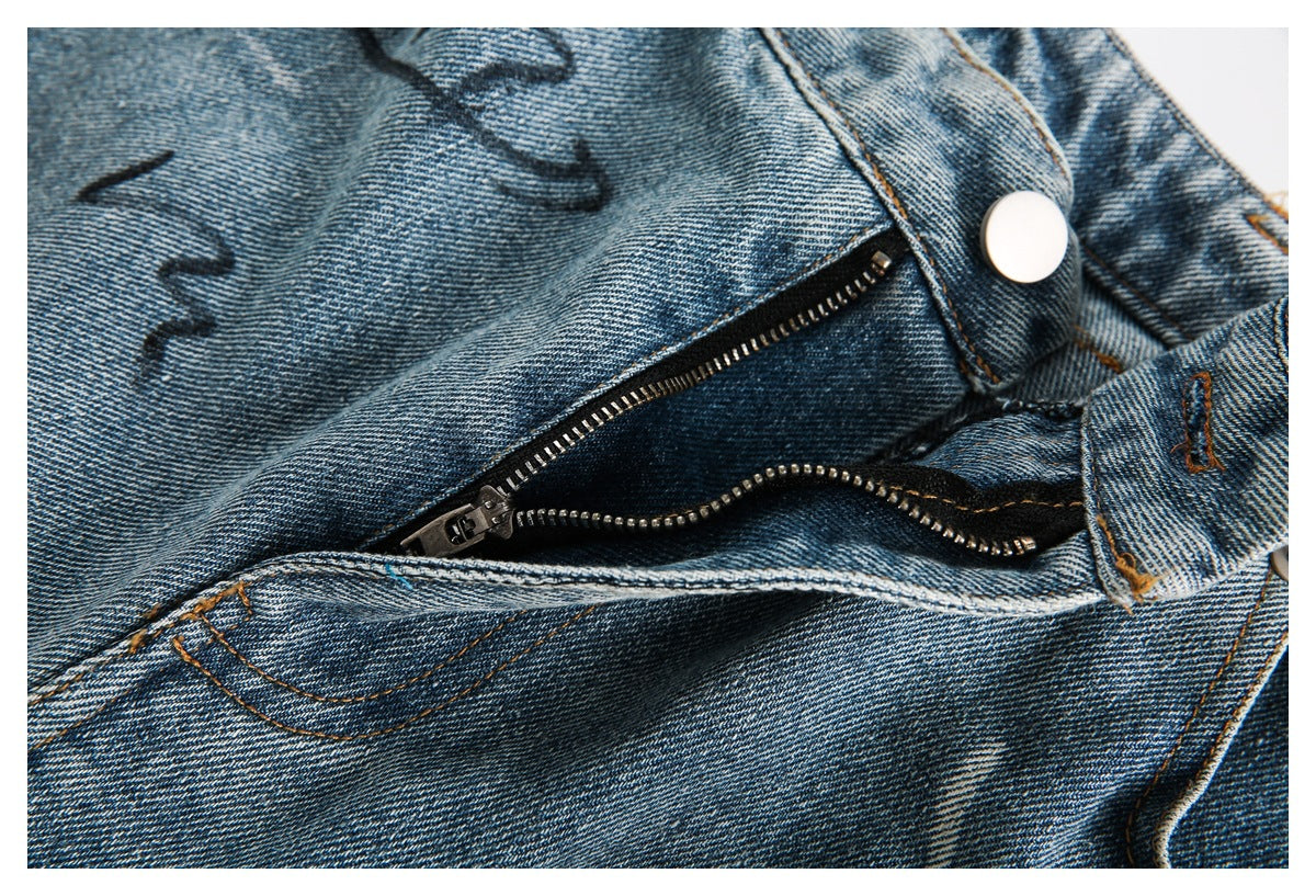 Close-up of the jeans' open metal zipper and button on washed blue denim.
