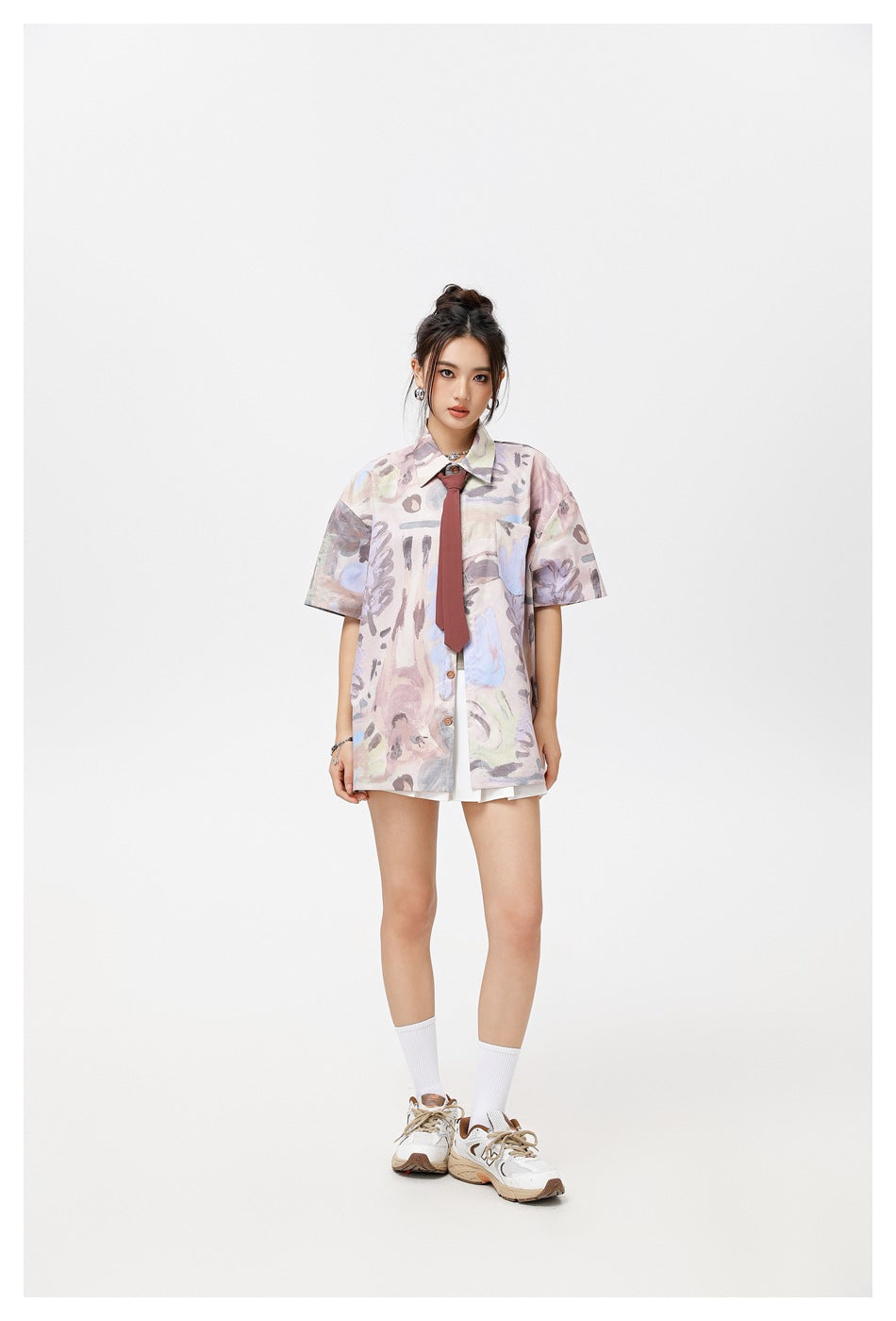 Model wearing pink-purple abstract print short-sleeve shirt with burgundy necktie and white pleated skirt