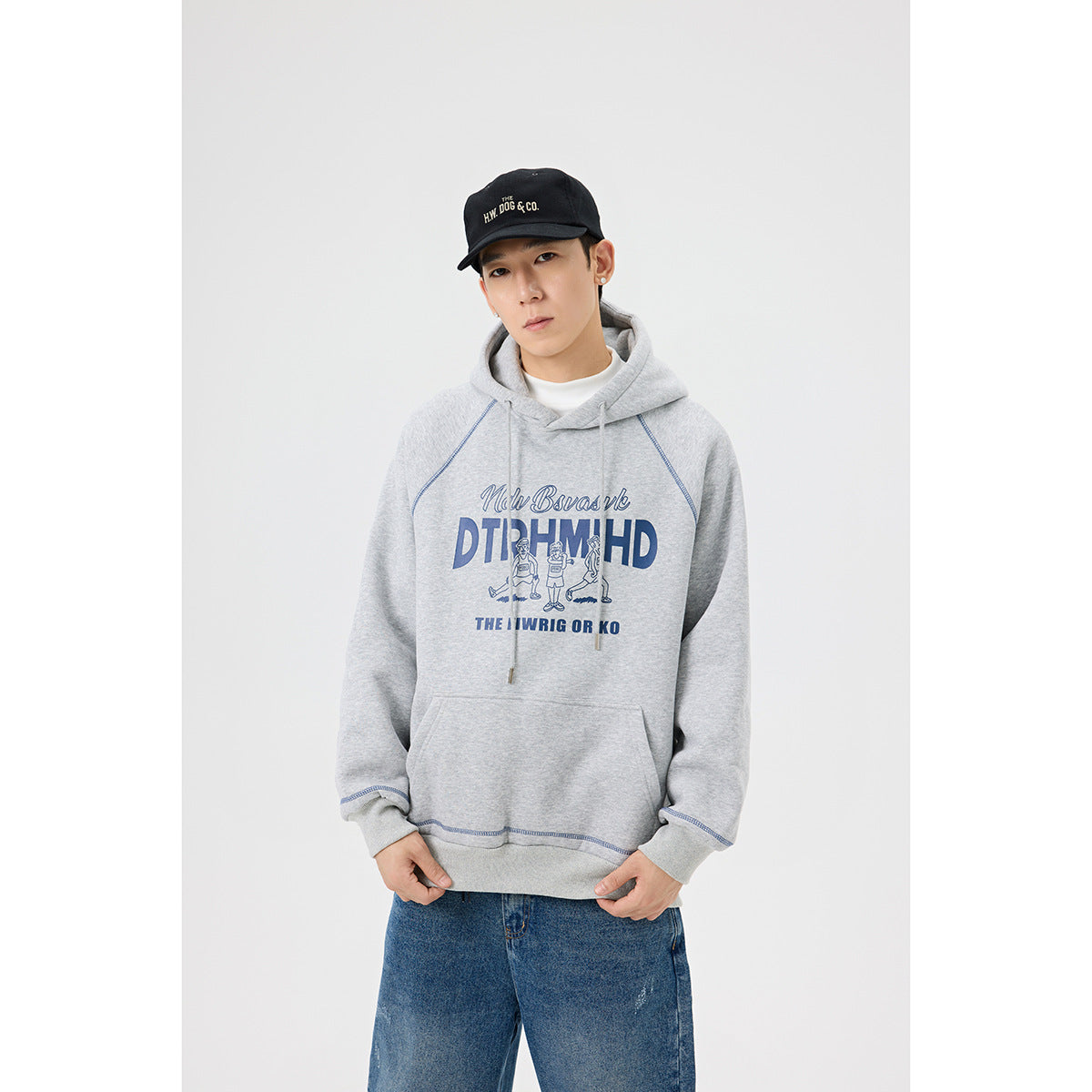 Model wearing a light gray hooded sweatshirt with blue chest graphic and seam accents, paired with blue jeans.