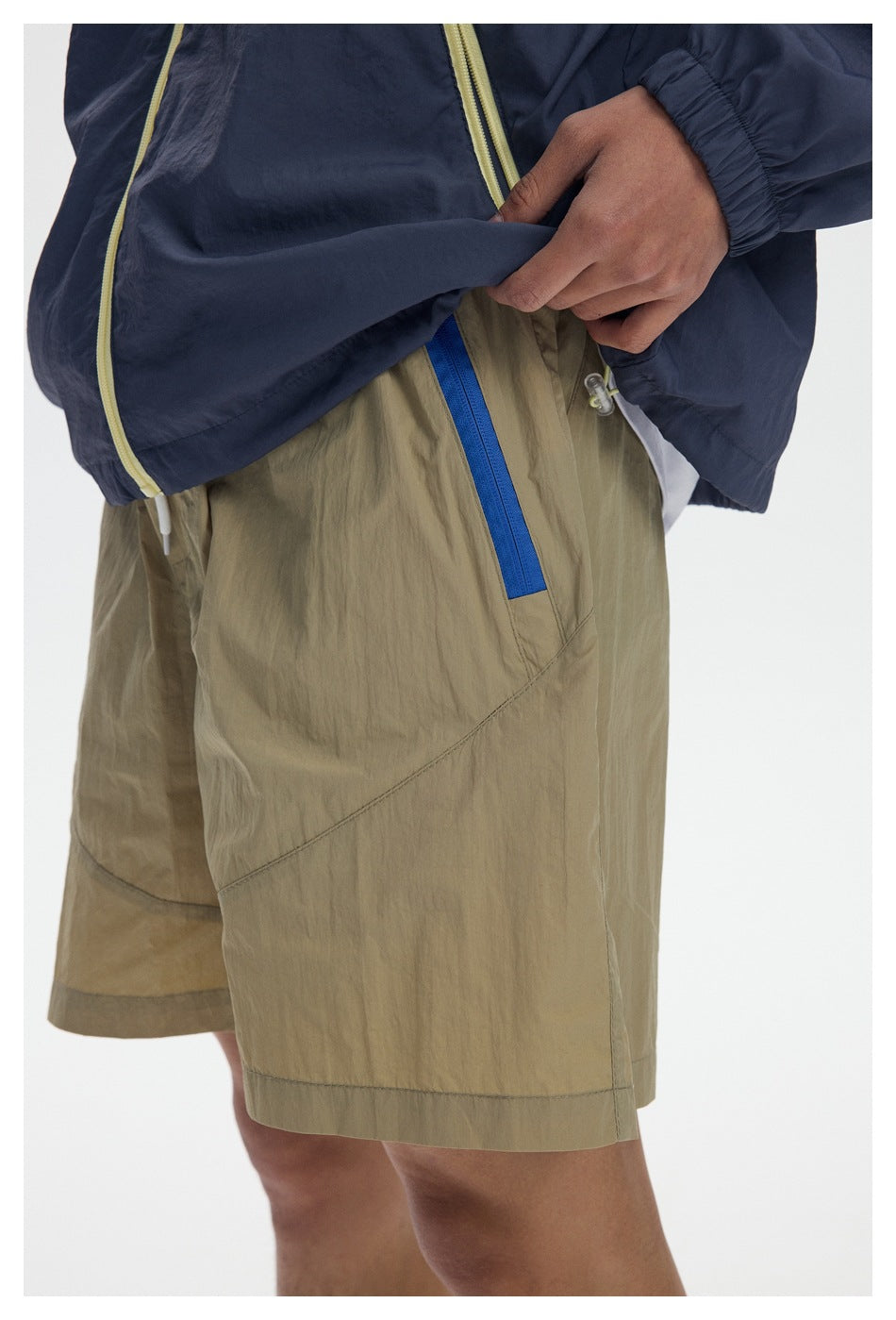Close-up of khaki shorts with a bright blue pocket zipper, shown beneath a navy jacket.