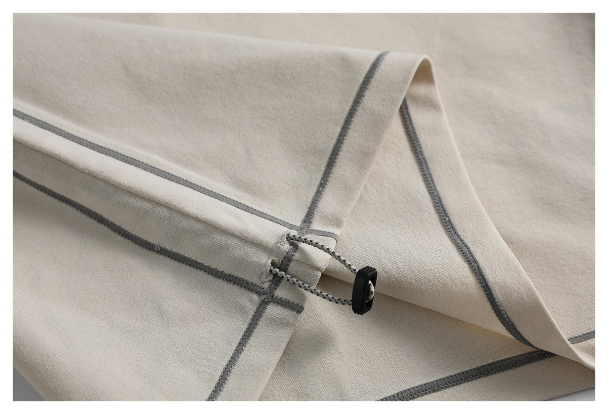 Close-up of a light beige garment hem with gray stitching and an adjustable cord toggle.