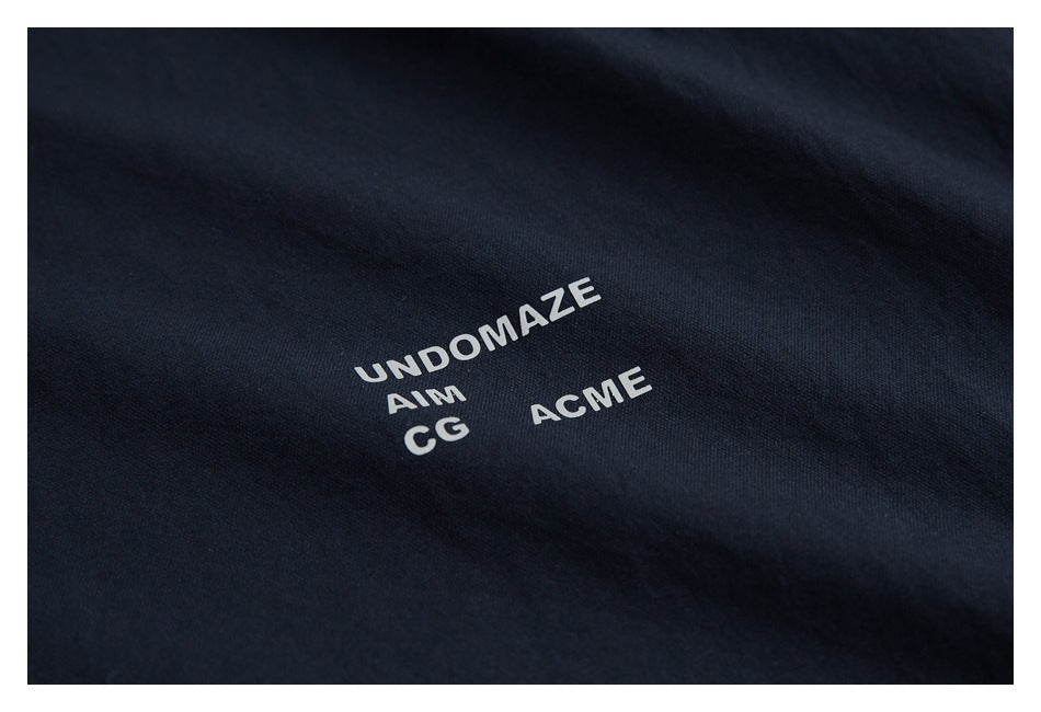 Close-up of navy fabric with small white printed words: “UND OMAZE,” “AIM,” “CG,” and “ACME.”