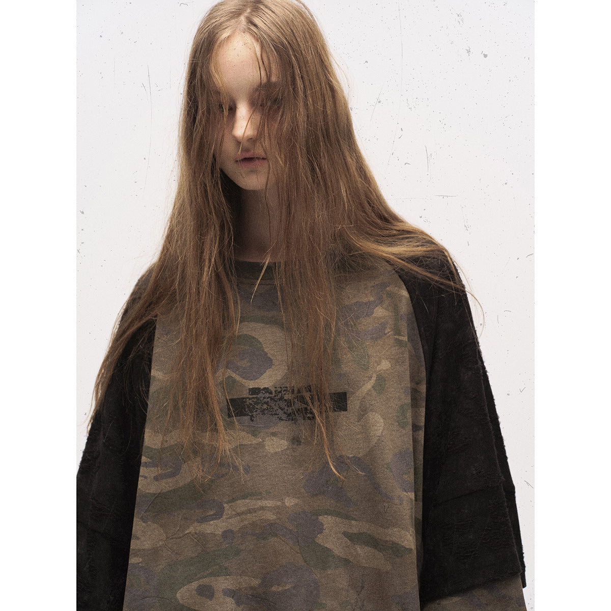 Close view of a model wearing an olive camouflage raglan top with black sleeves and a distressed dark chest graphic.