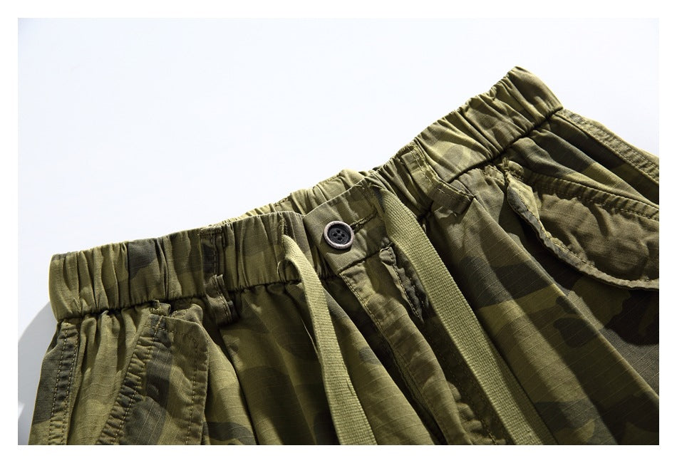 Close-up of the camouflage shorts' elastic waistband, button closure, drawstring, and front pocket.