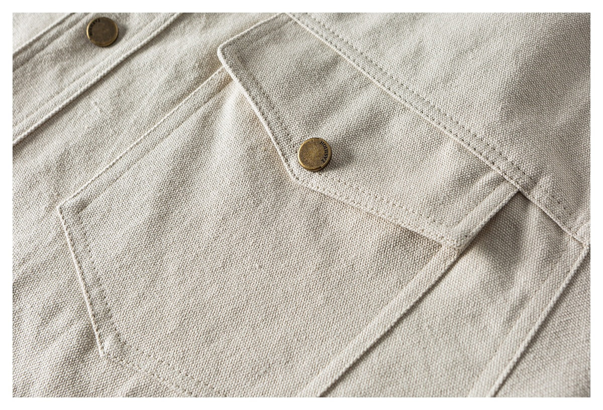 Close-up of a beige shirt chest pocket with a flap and brass button.
