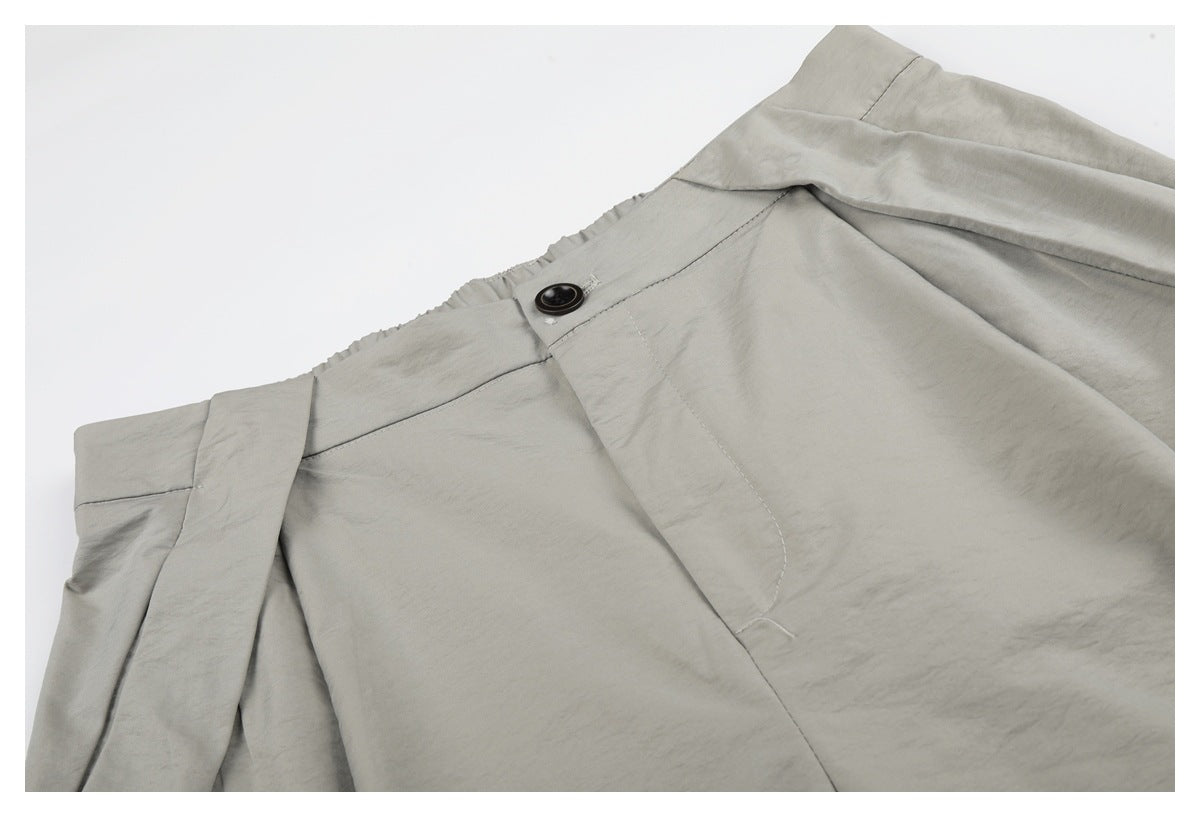 Close-up of light gray shorts showing the waistband, dark button, fly, and front pleat.