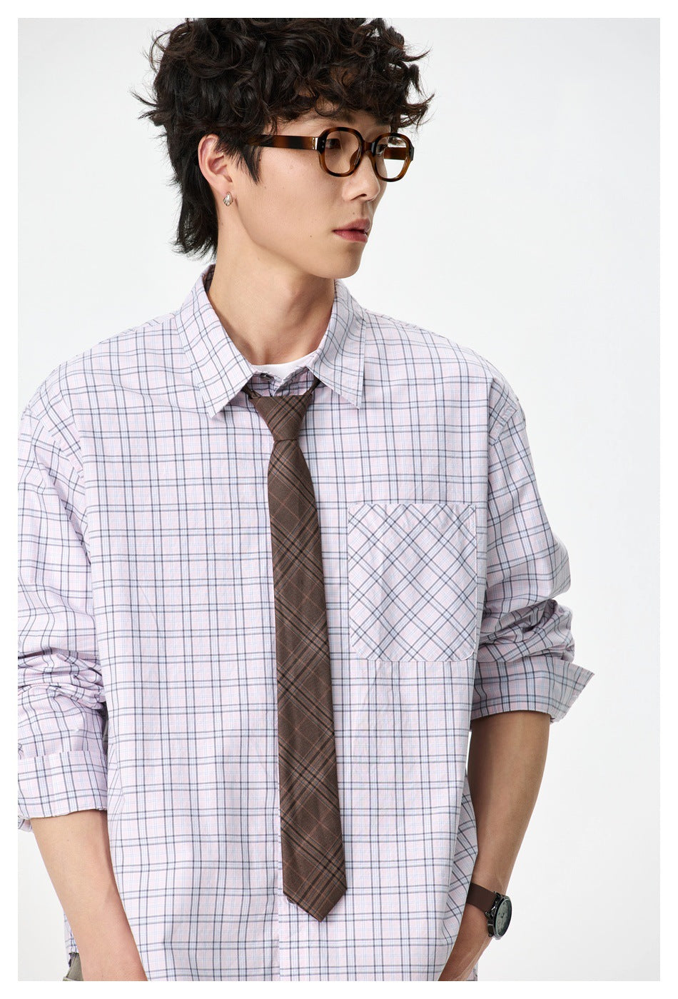 Close view of a model wearing a pale lavender plaid button-down shirt with a diagonally plaid chest pocket and brown tie.