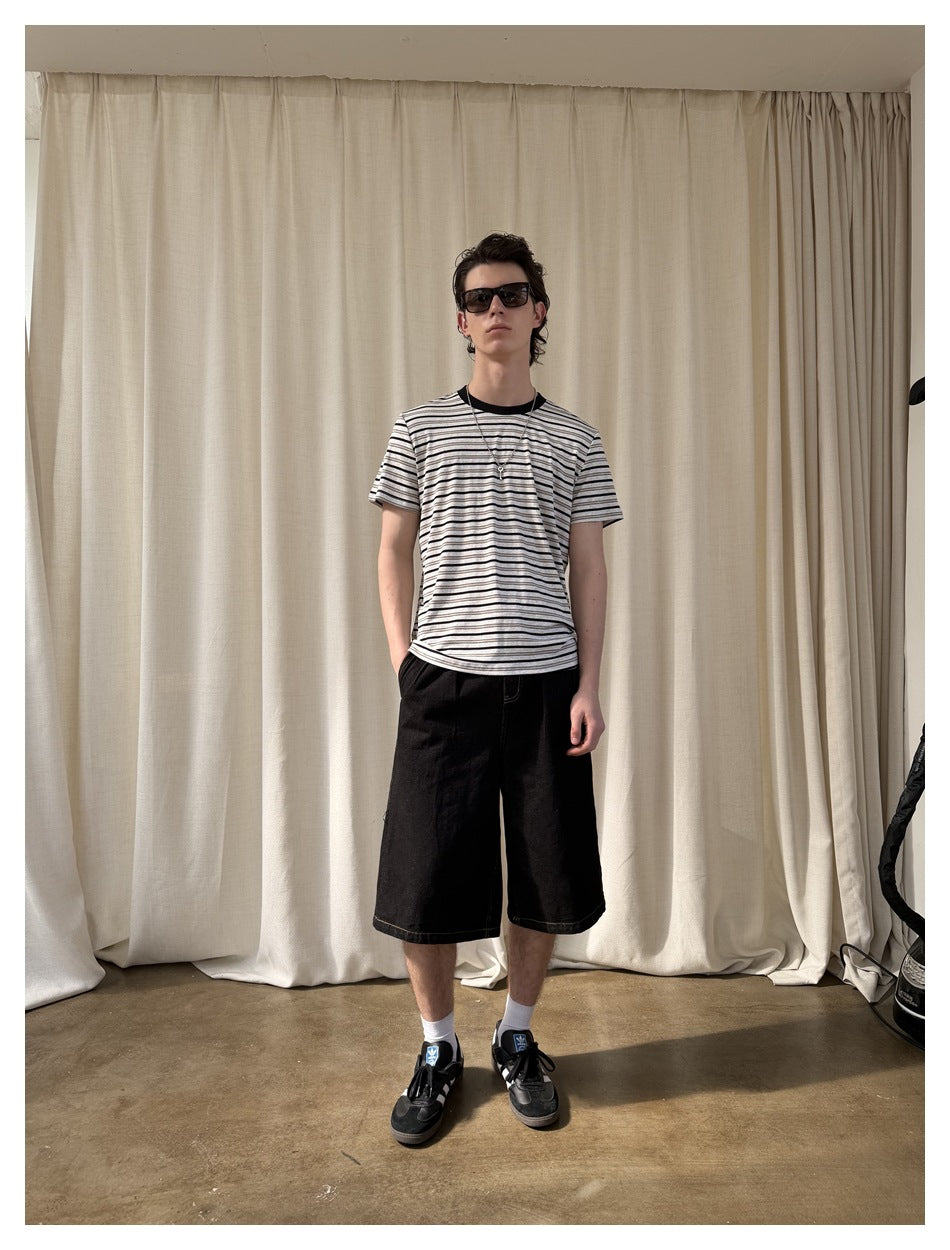 Front view of a model wearing a white T-shirt with thin dark horizontal stripes and loose black shorts.