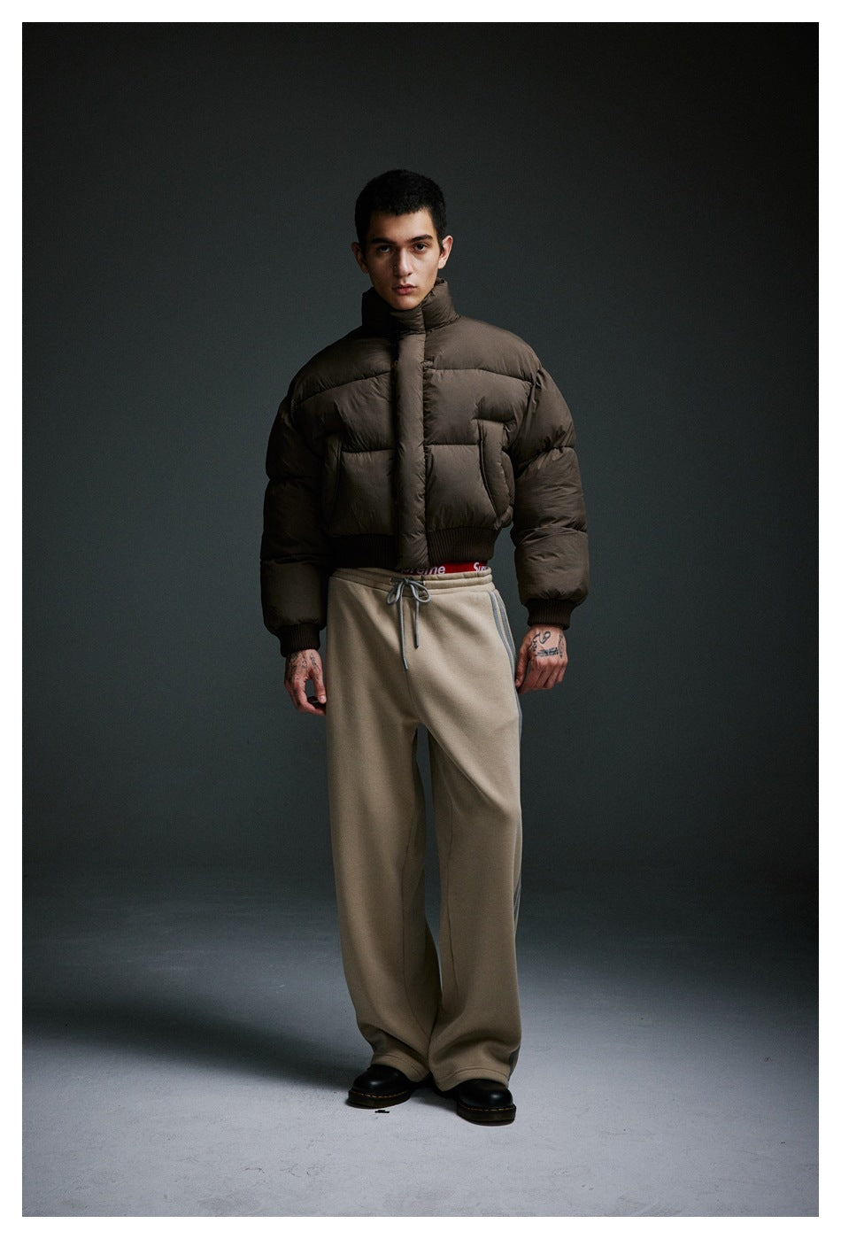 Model wearing a cropped dark brown puffer jacket and loose taupe drawstring trousers.