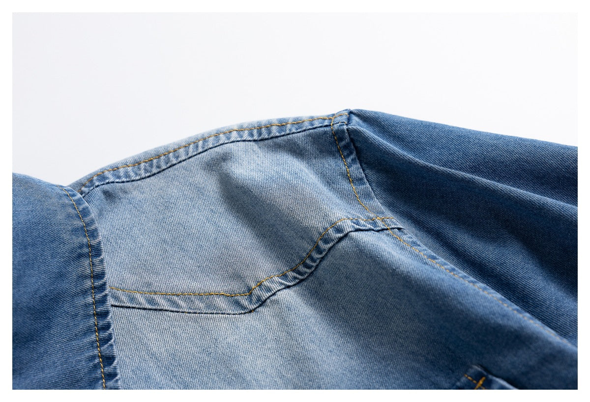 Close-up of a blue denim shirt shoulder seam with contrasting tan stitching and faded wash.