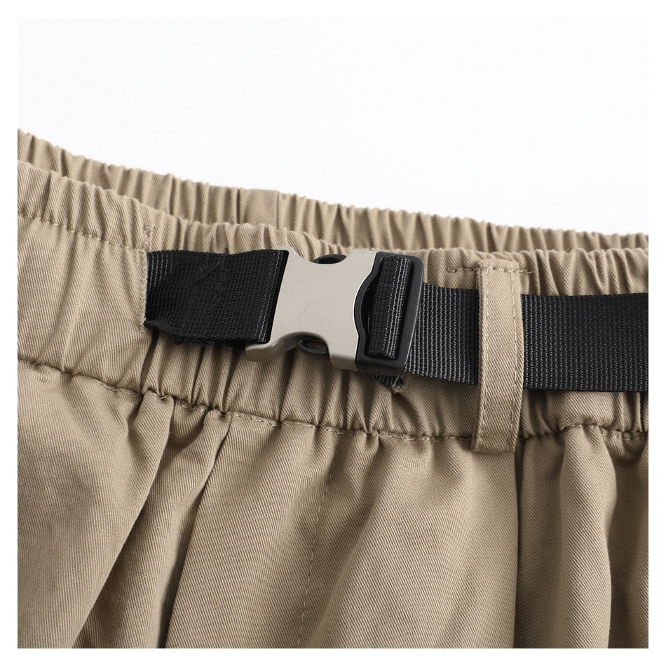 Close-up of the trousers' elastic waistband and black belt with a plastic buckle and fabric loop.