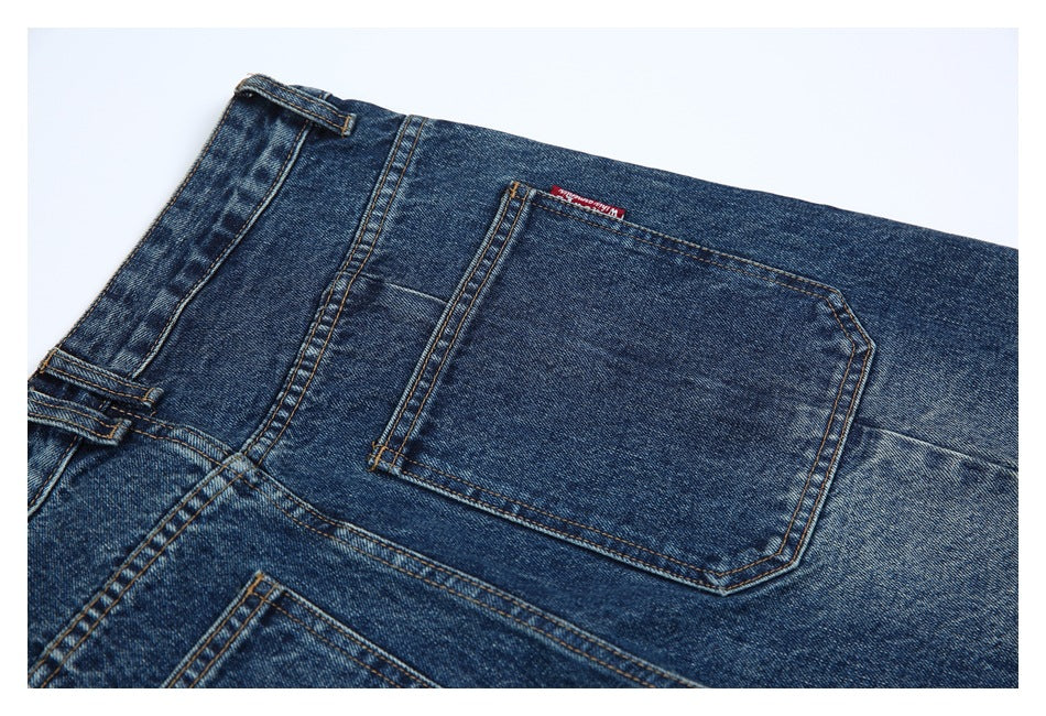 Close-up of dark indigo jeans showing the back pocket, waistband, belt loops, and a small red woven tab.