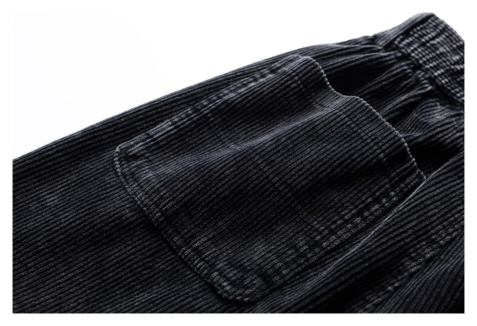 Close-up of a patch pocket and waistband on black ribbed corduroy trousers.