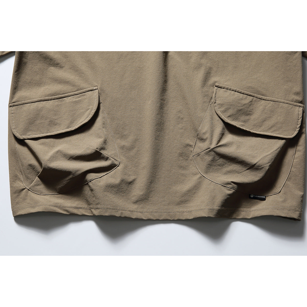 Close-up of two large flap pockets on the lower front of a taupe shirt.