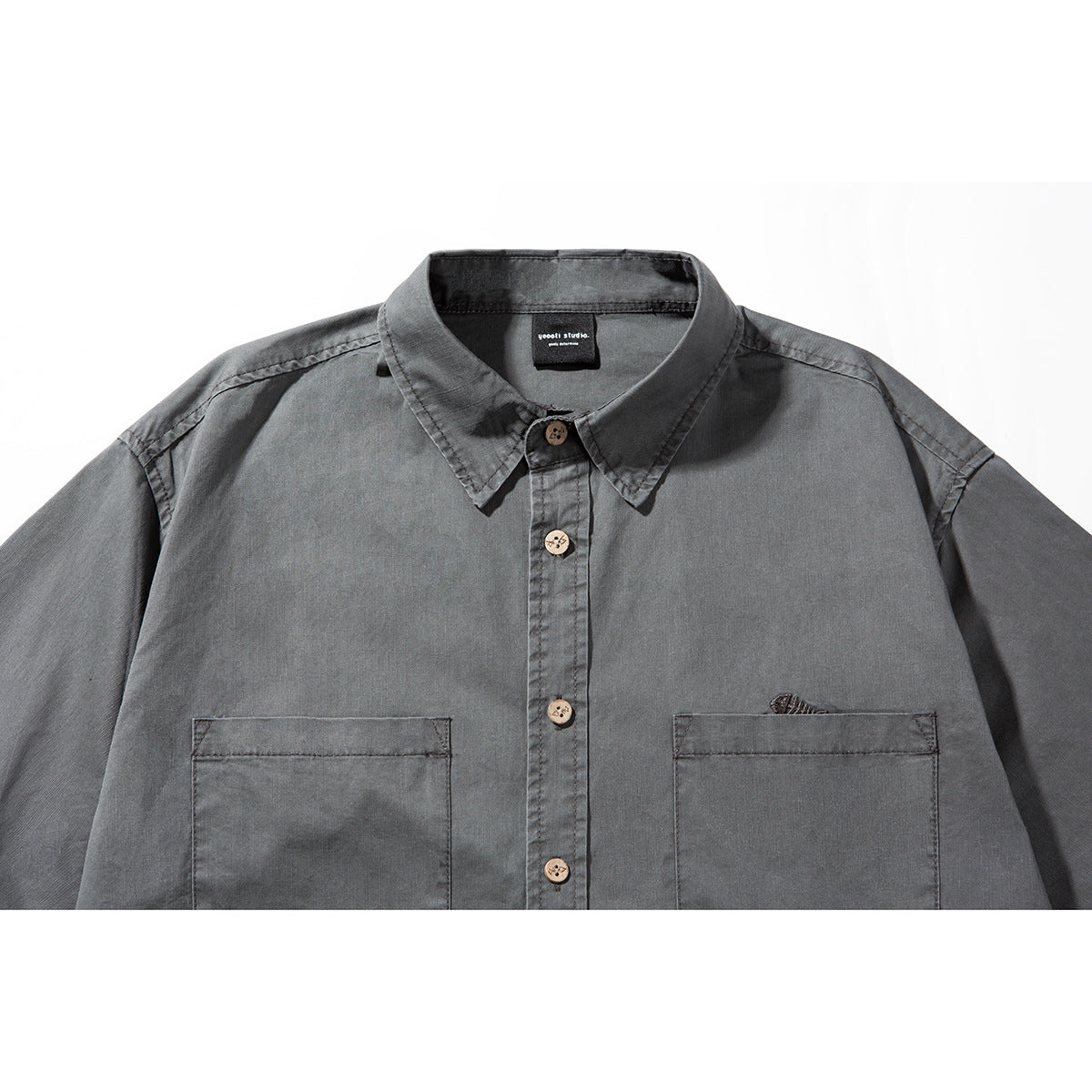 Close view of a charcoal-gray short-sleeve button-up shirt with a pointed collar, wooden buttons, and two chest pockets.