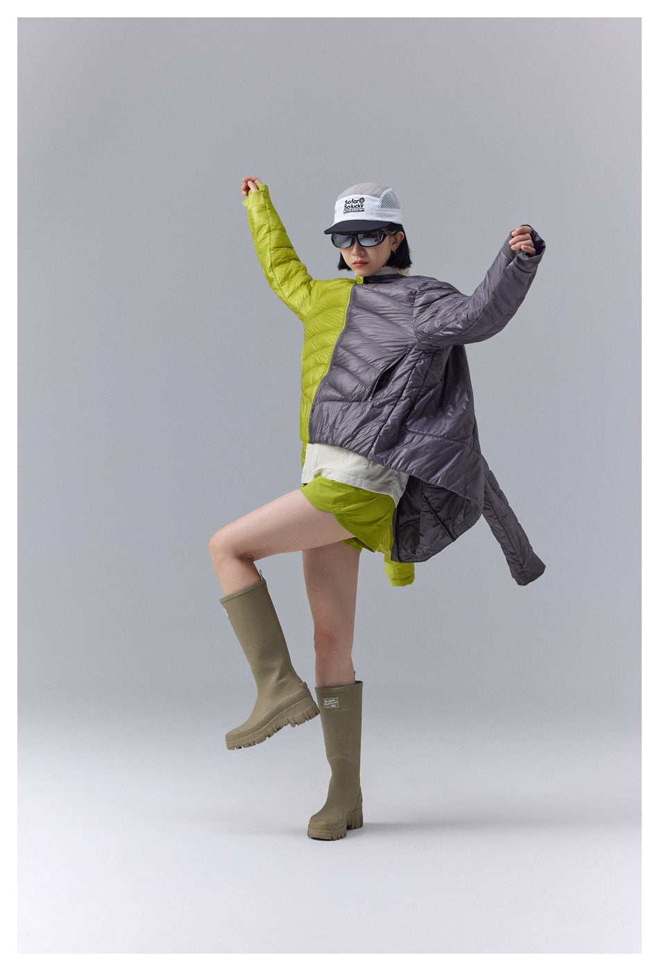 Model wearing a two-tone lime and charcoal quilted jacket, shorts, sunglasses, and a cap.
