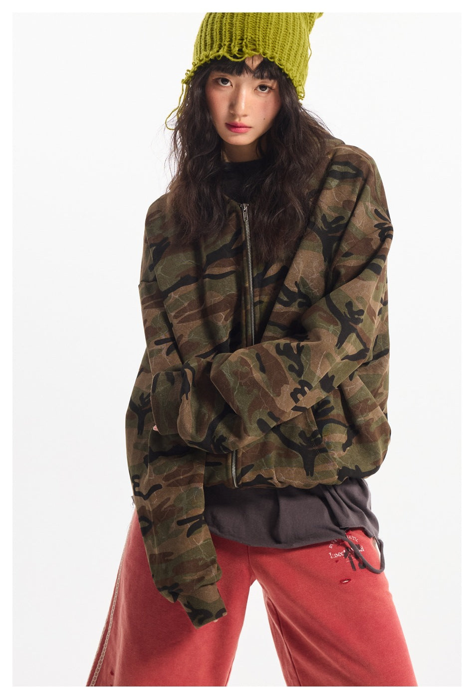 Close view of a model wearing an oversized brown and olive camouflage zip jacket with ribbed cuffs.