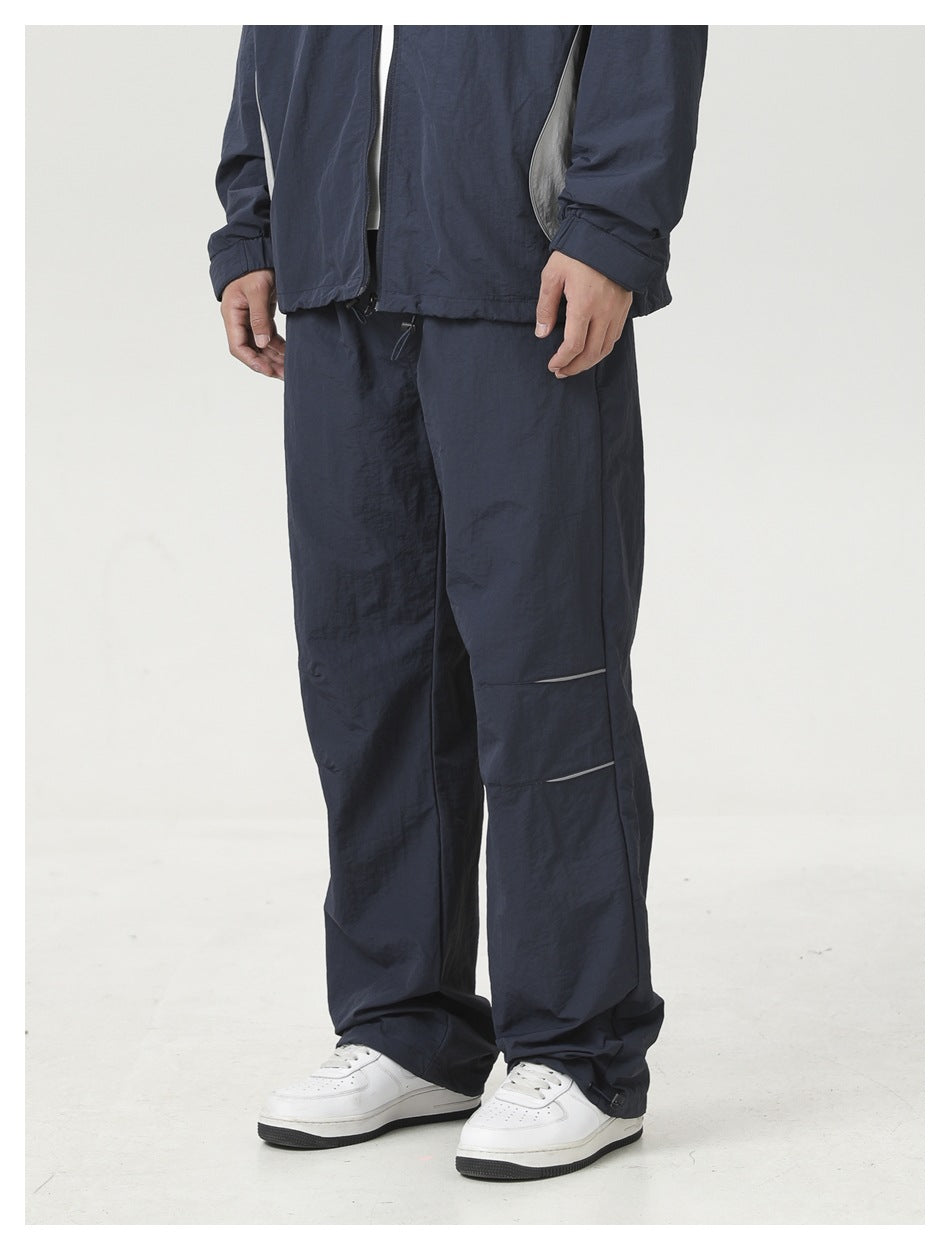 Cropped front view of a model wearing loose navy pants with reflective calf accents and white sneakers.