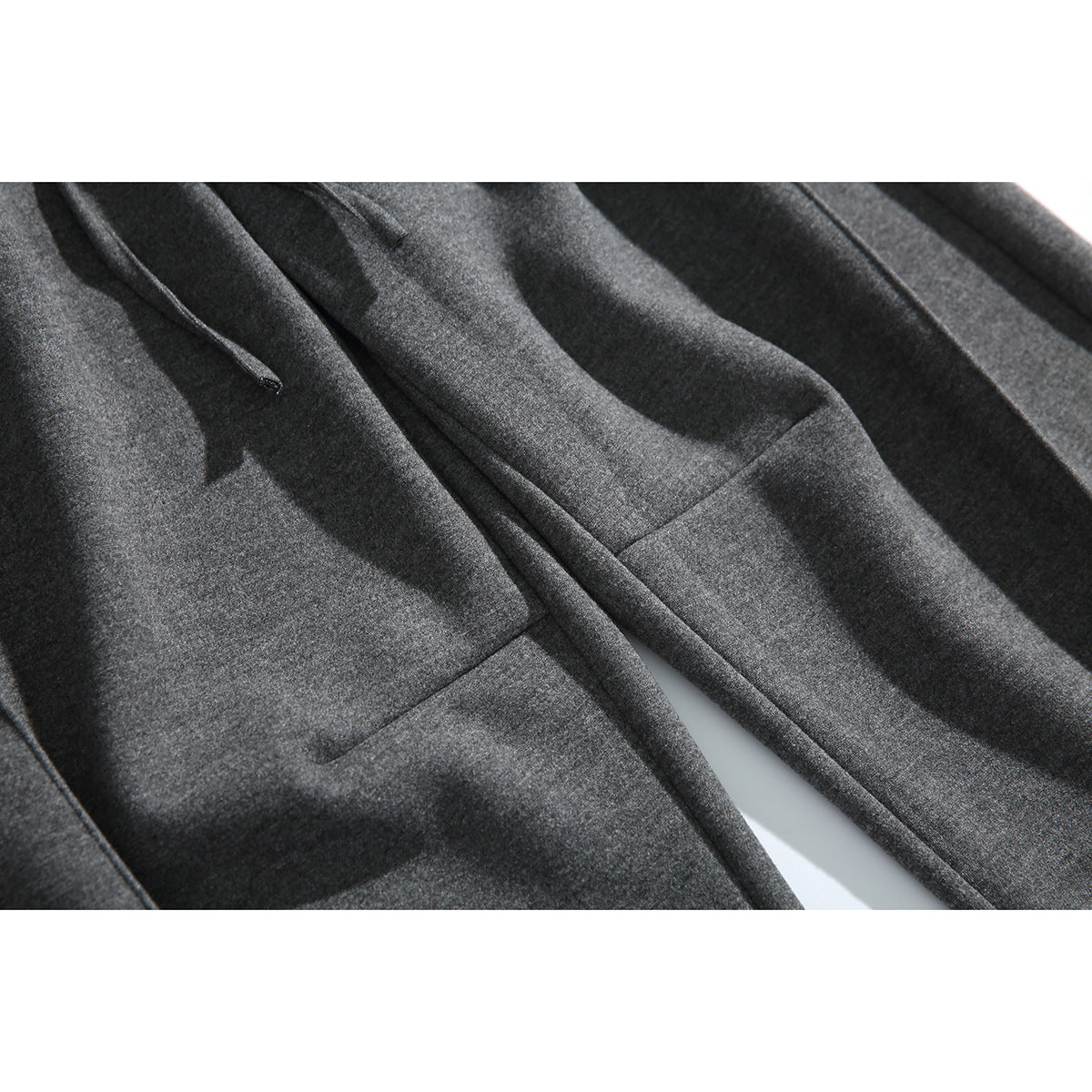 Close-up of charcoal pants showing a front pocket, drawstring, and fabric texture.