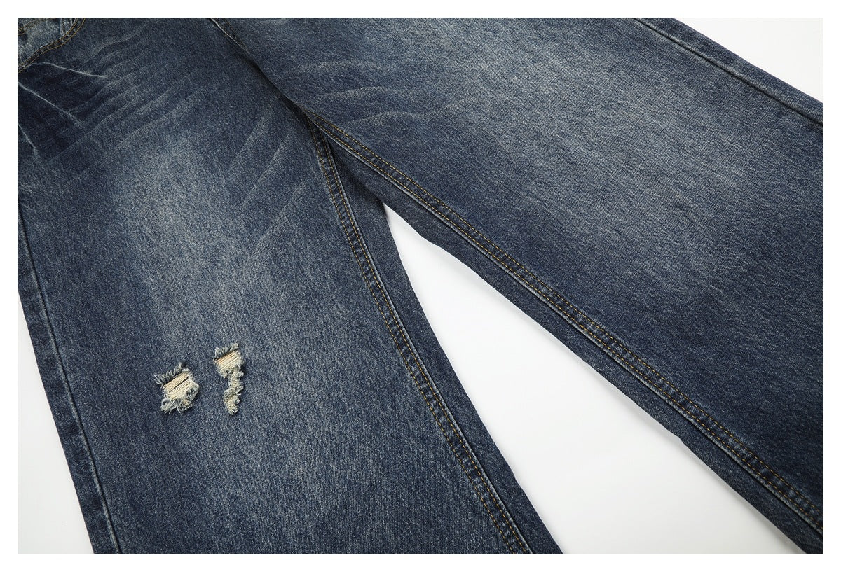 Close-up of dark blue jeans with two small distressed tears and contrast stitching.