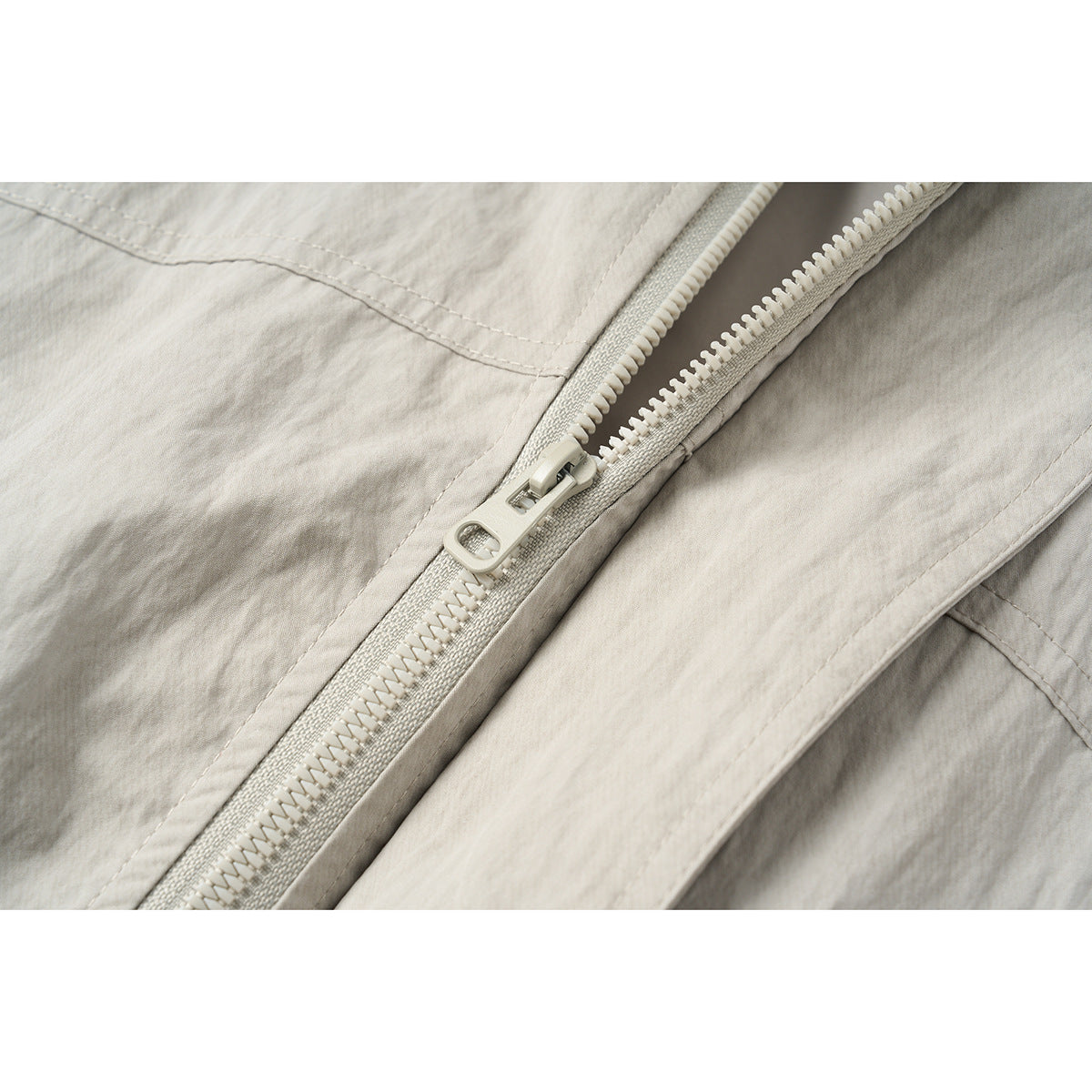 Close-up of a pale zipper and stitching on the light gray-beige jacket.