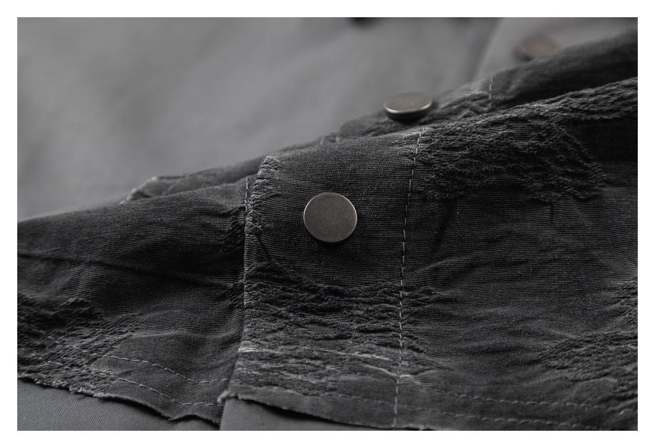 Close-up of a dark gray textured shirt panel with stitching and a round metal snap button.