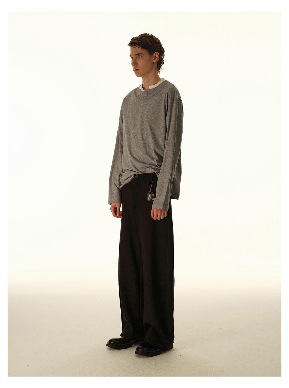 Side view of a model wearing a gray long-sleeve henley over a white shirt with wide black trousers.