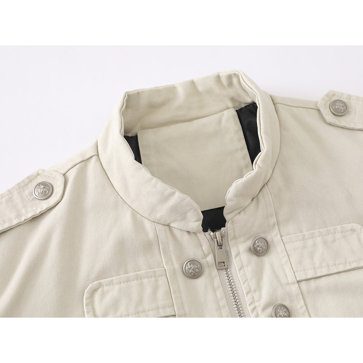 Close-up of an ivory jacket's stand collar, front zipper, embossed buttons, shoulder tabs and flap pockets.