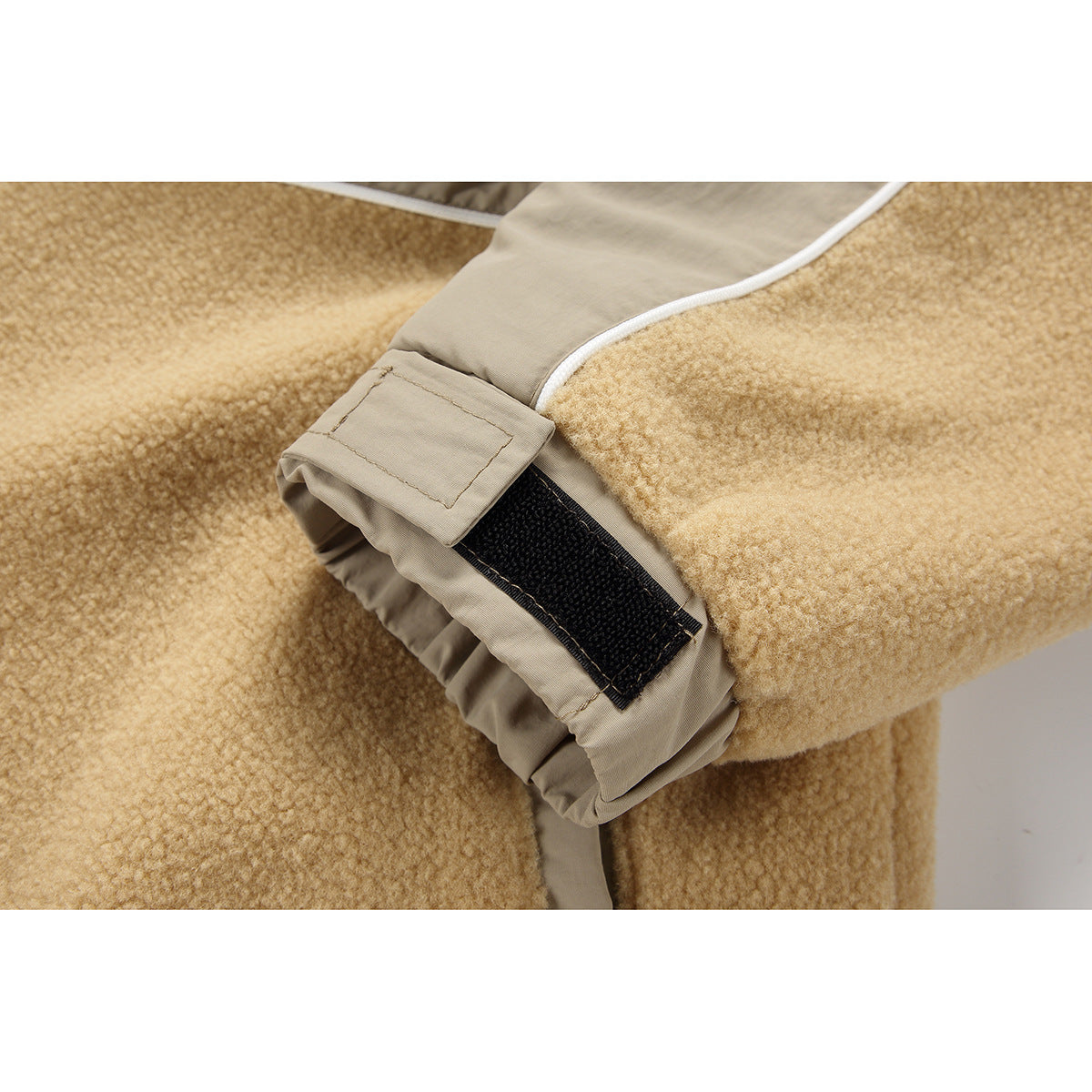 Close-up of a beige cuff tab with black hook-and-loop closure against tan fleece.