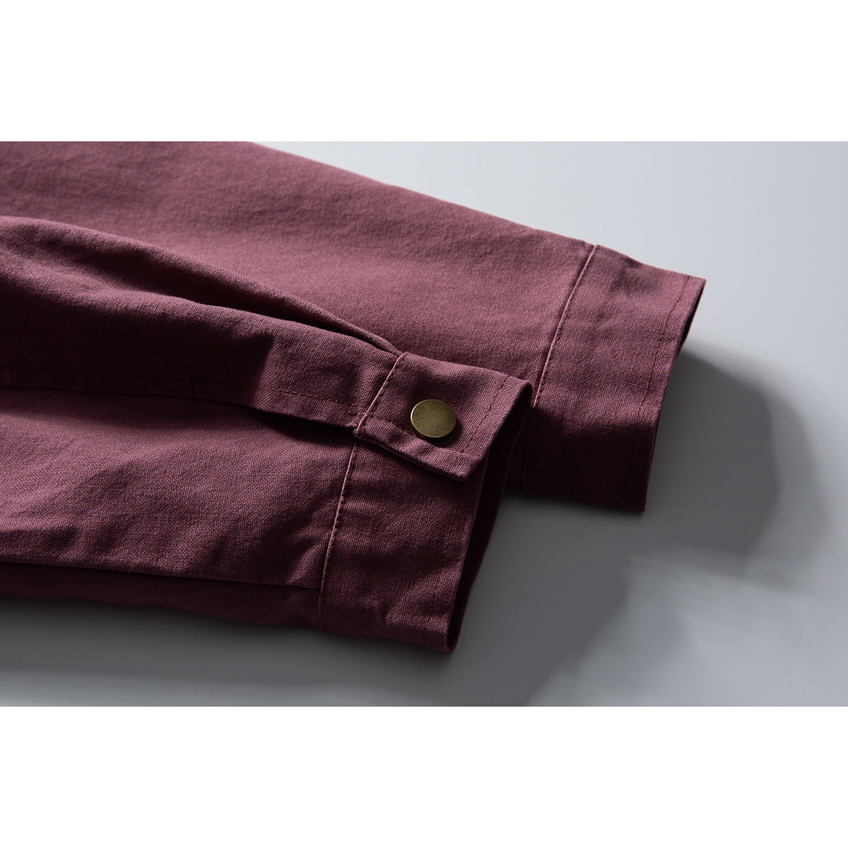 Close-up of a burgundy jacket sleeve and cuff, showing a snap-button tab.