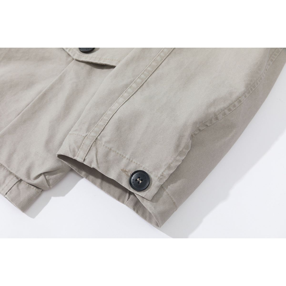Close-up of a light gray-beige jacket sleeve cuff with a dark button and stitched seam.
