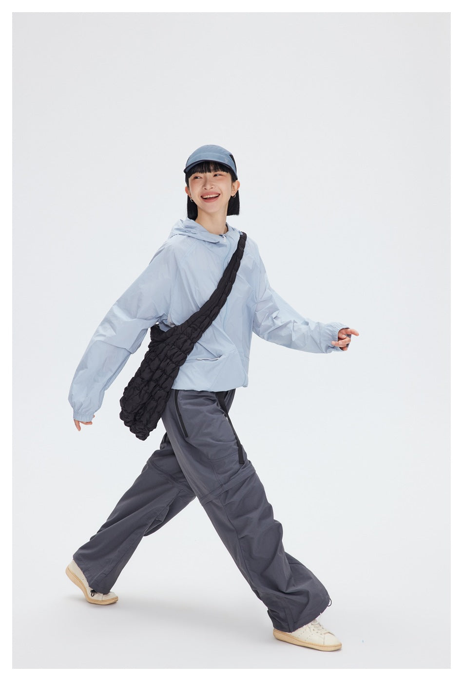 Model walking in a pale blue hooded jacket and dark wide-leg pants, carrying a black crossbody bag.